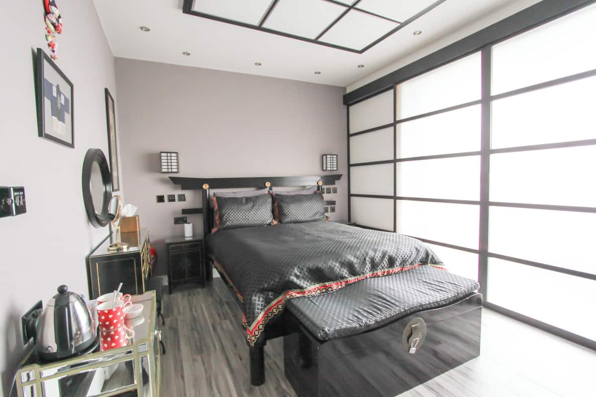 A modern bedroom with a bed, bedside tables, a mirror, and a window.