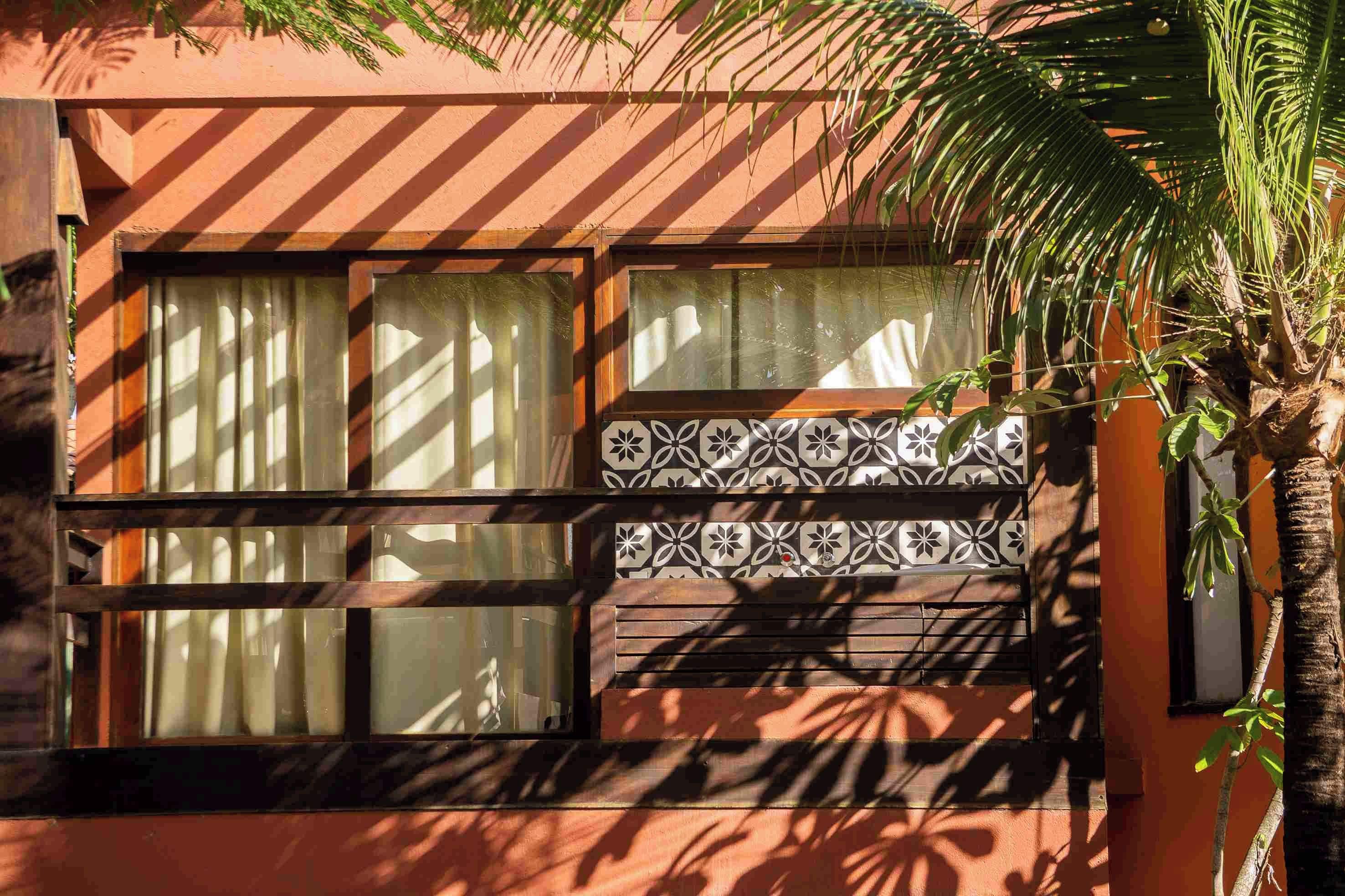 Um edifício com uma janela e um design de azulejos padronizado, além de uma palmeira ao primeiro plano.