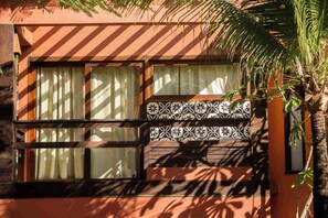 A building with a window featuring a patterned tile design and a palm tree in the foreground. - Pousada Naquela (Jijoca de Jericoacoara)