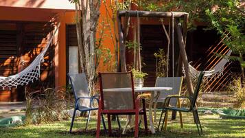 Una hamaca, una mesa y sillas en un jardín, con un edificio al fondo.
