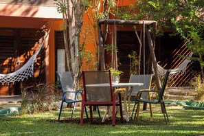 Una hamaca, una mesa y sillas en un jardín, con un edificio al fondo.