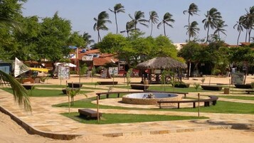 Resort tropical com um elemento central de água circular, rodeado por palmeiras e um bangalô com telhado de palha.