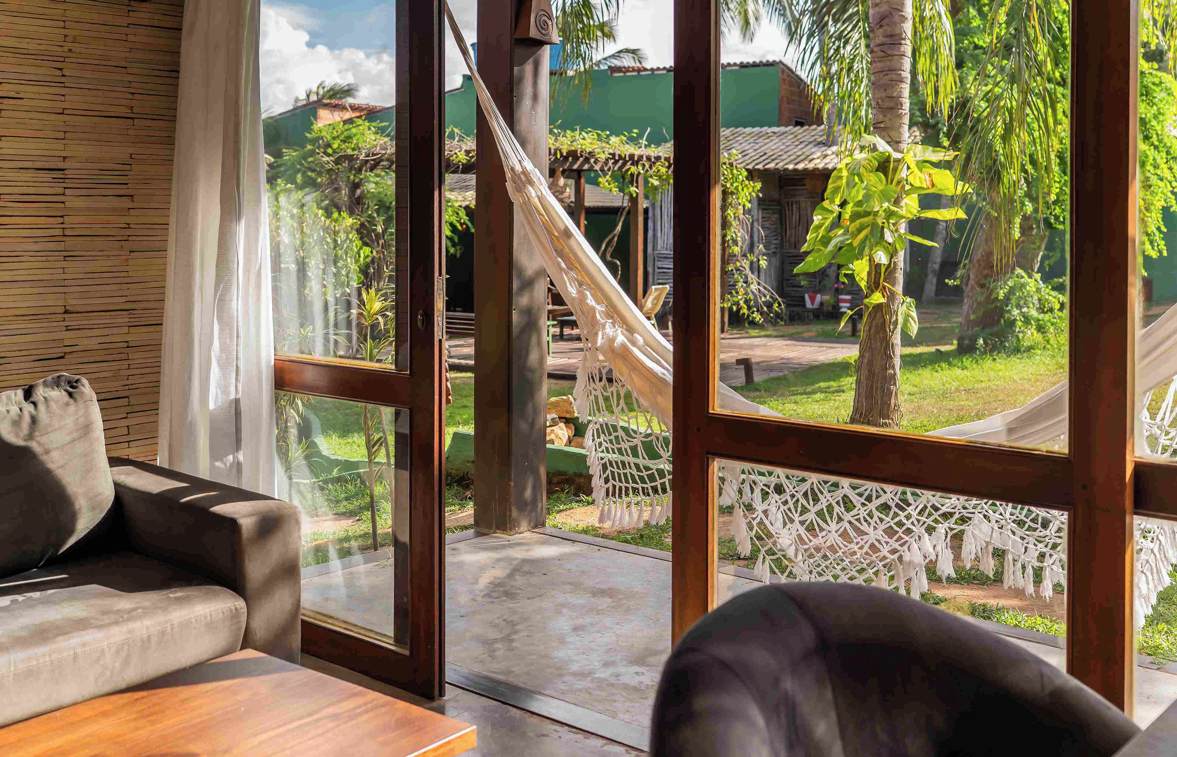 Una habitación con un ventanal grande, una hamaca y vistas a un jardín con una estructura de madera.