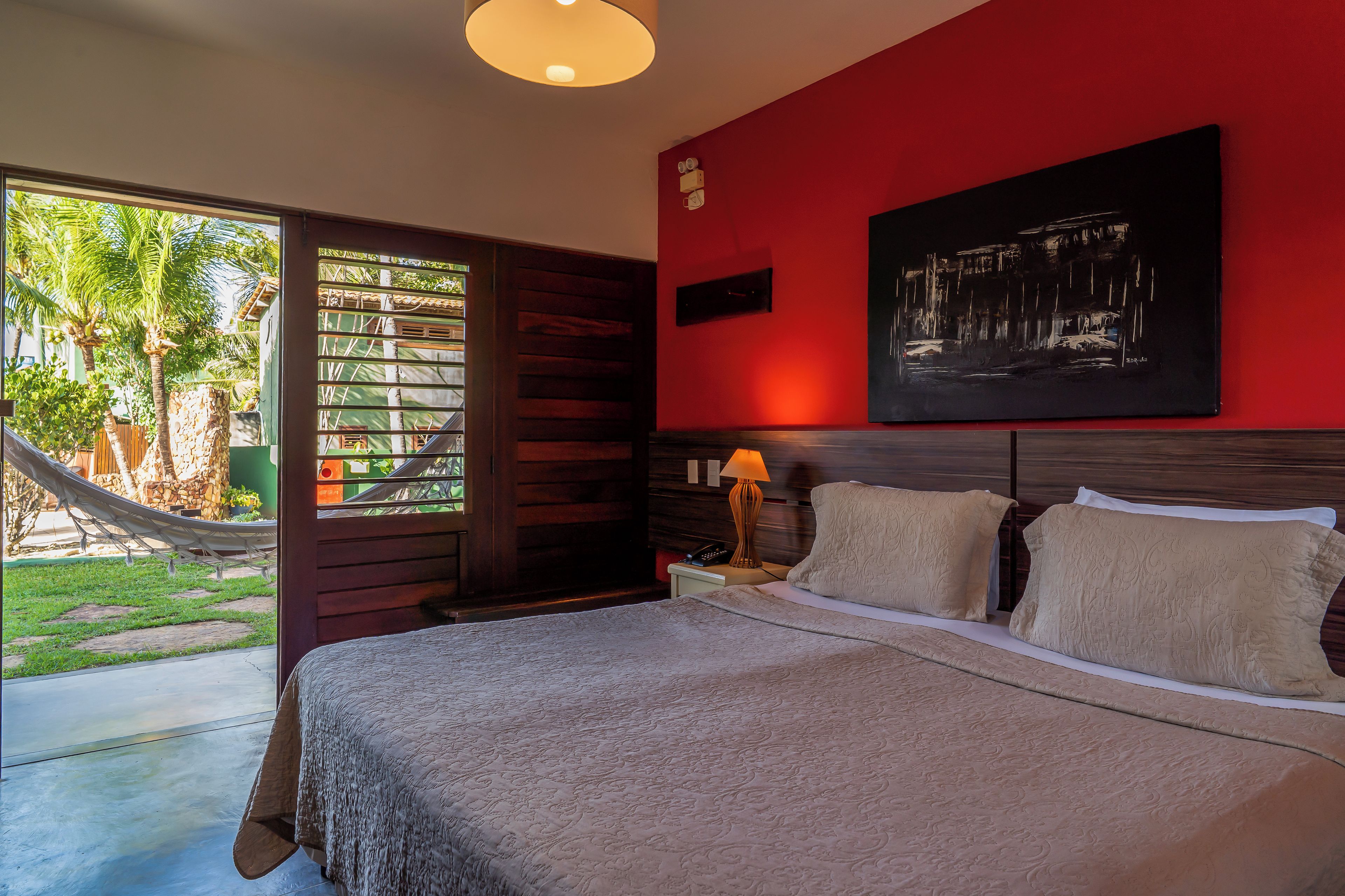Habitación de hotel con cama, mesita de noche, lámpara, un cuadro y vista al exterior.