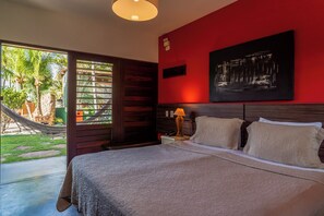 Habitación de hotel con cama, mesita de noche, lámpara, un cuadro y vista al exterior.