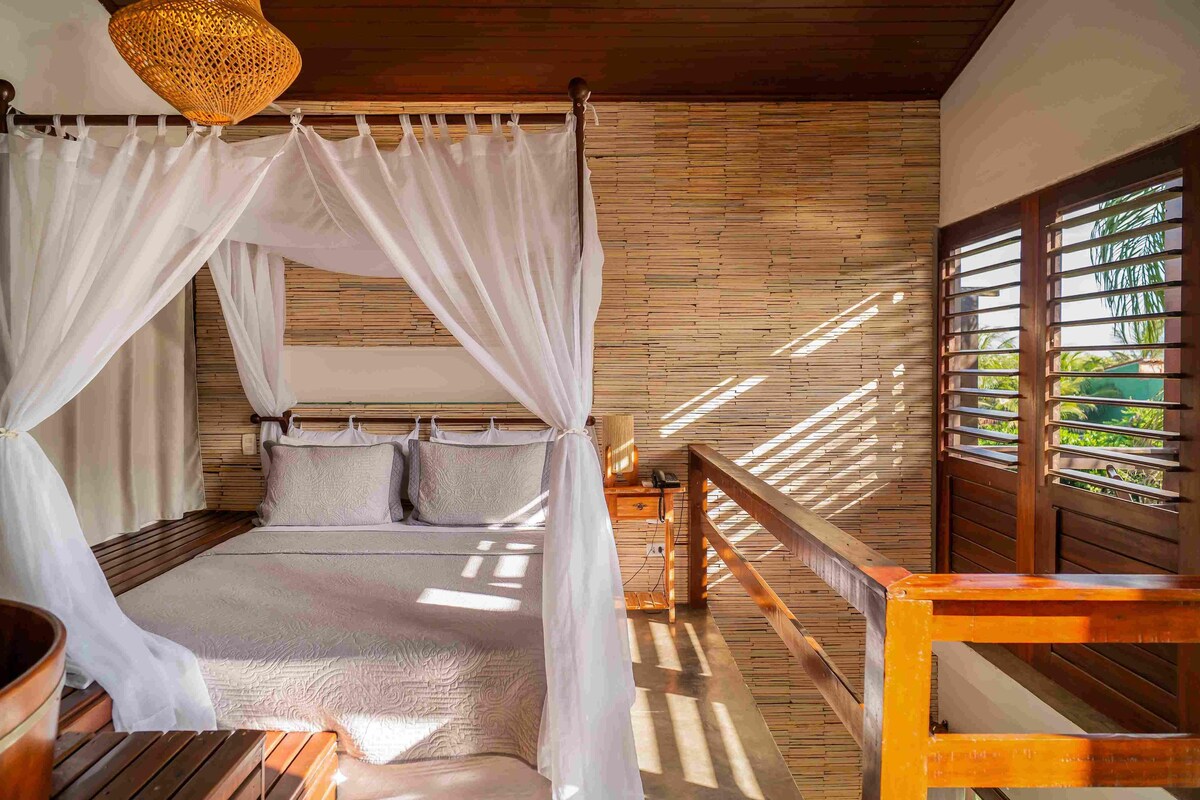 Una habitación con cama, piso de madera, lámpara de techo tejida y una ventana con persianas.