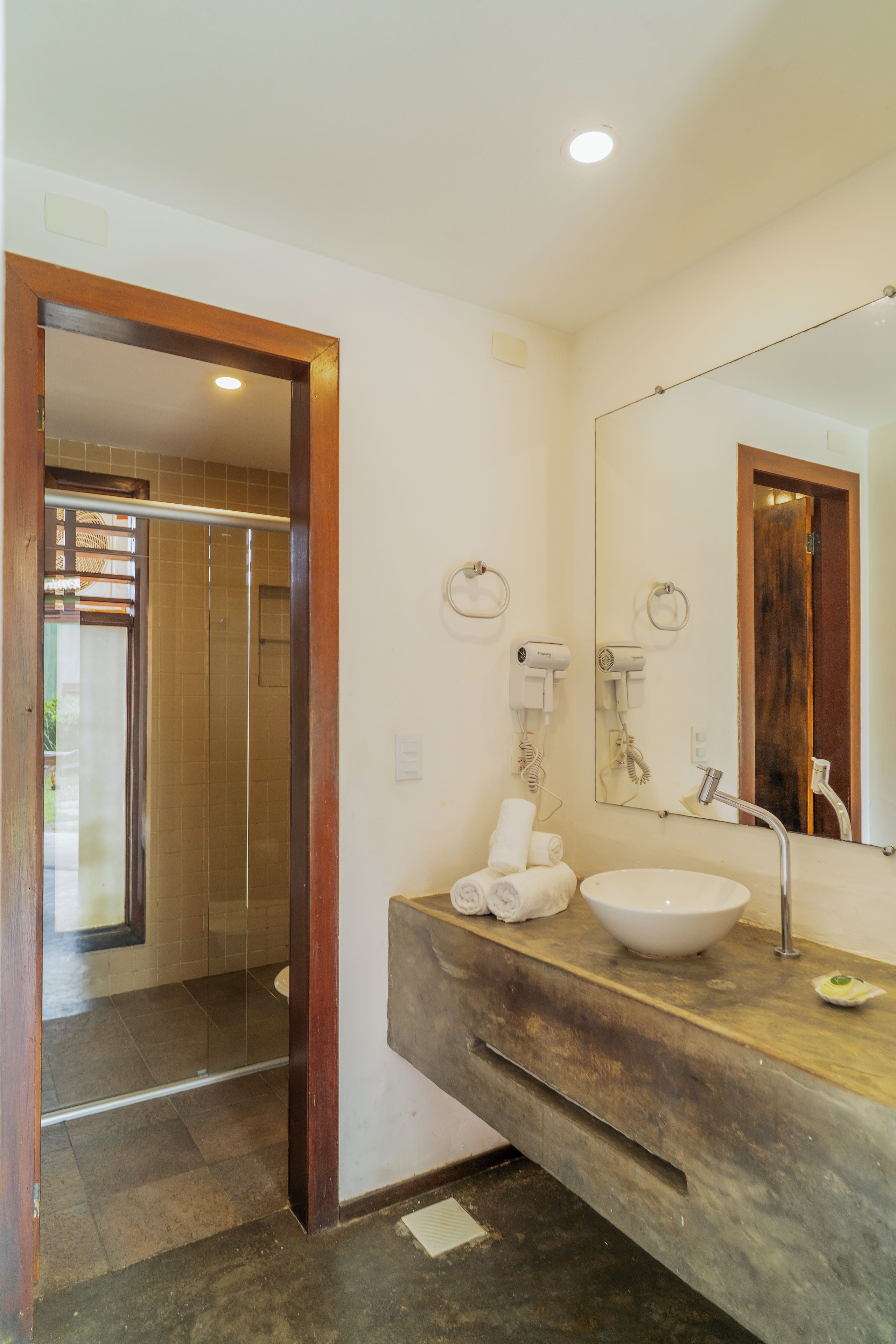 Un baño con tocador de madera, un lavabo, un espejo y una zona de ducha visible a través de una puerta abierta.