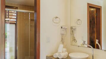 Un baño con tocador de madera, un lavabo, un espejo y una zona de ducha visible a través de una puerta abierta.
