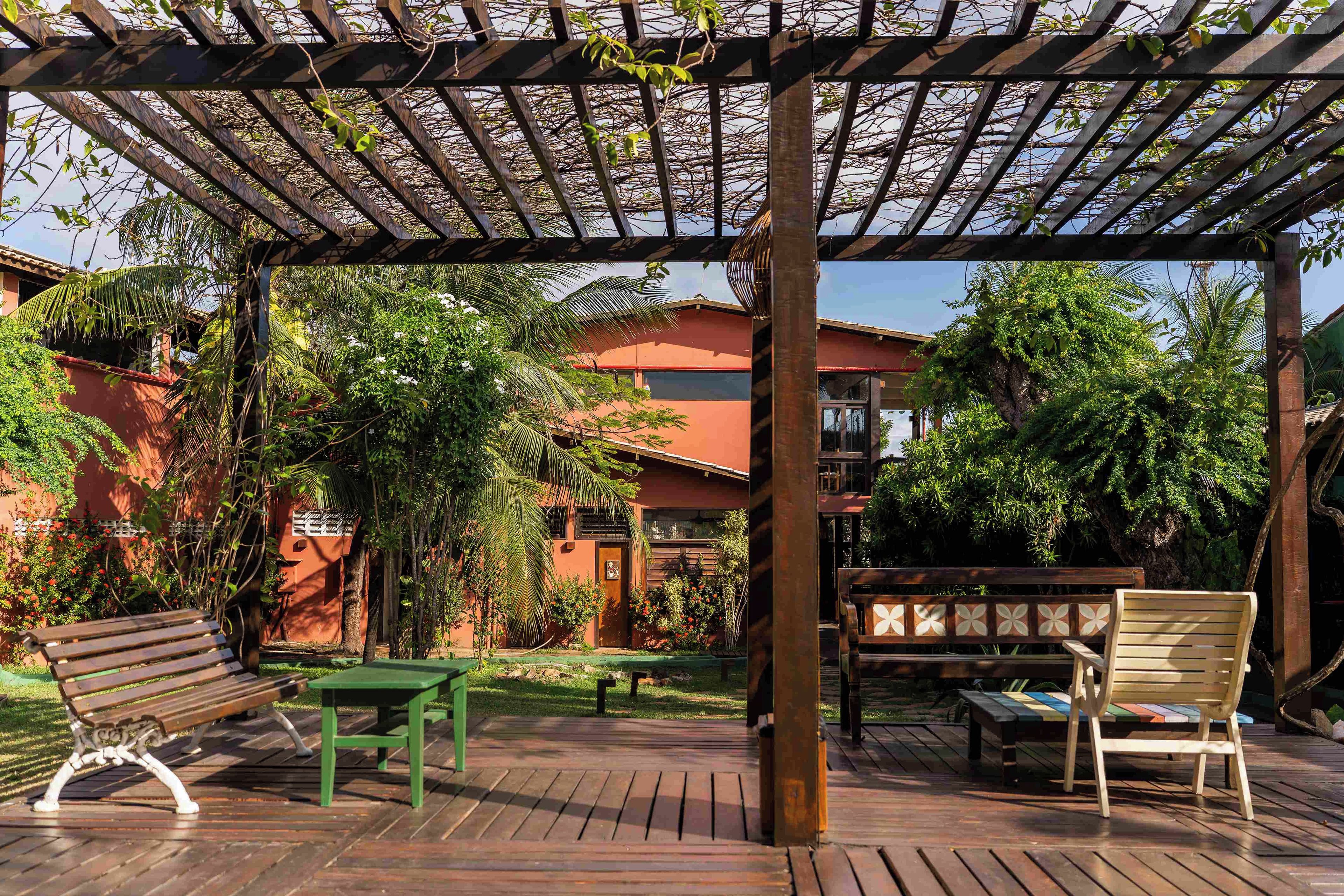 Una pérgola de madera con un jardín, una banca, una mesa y una silla.