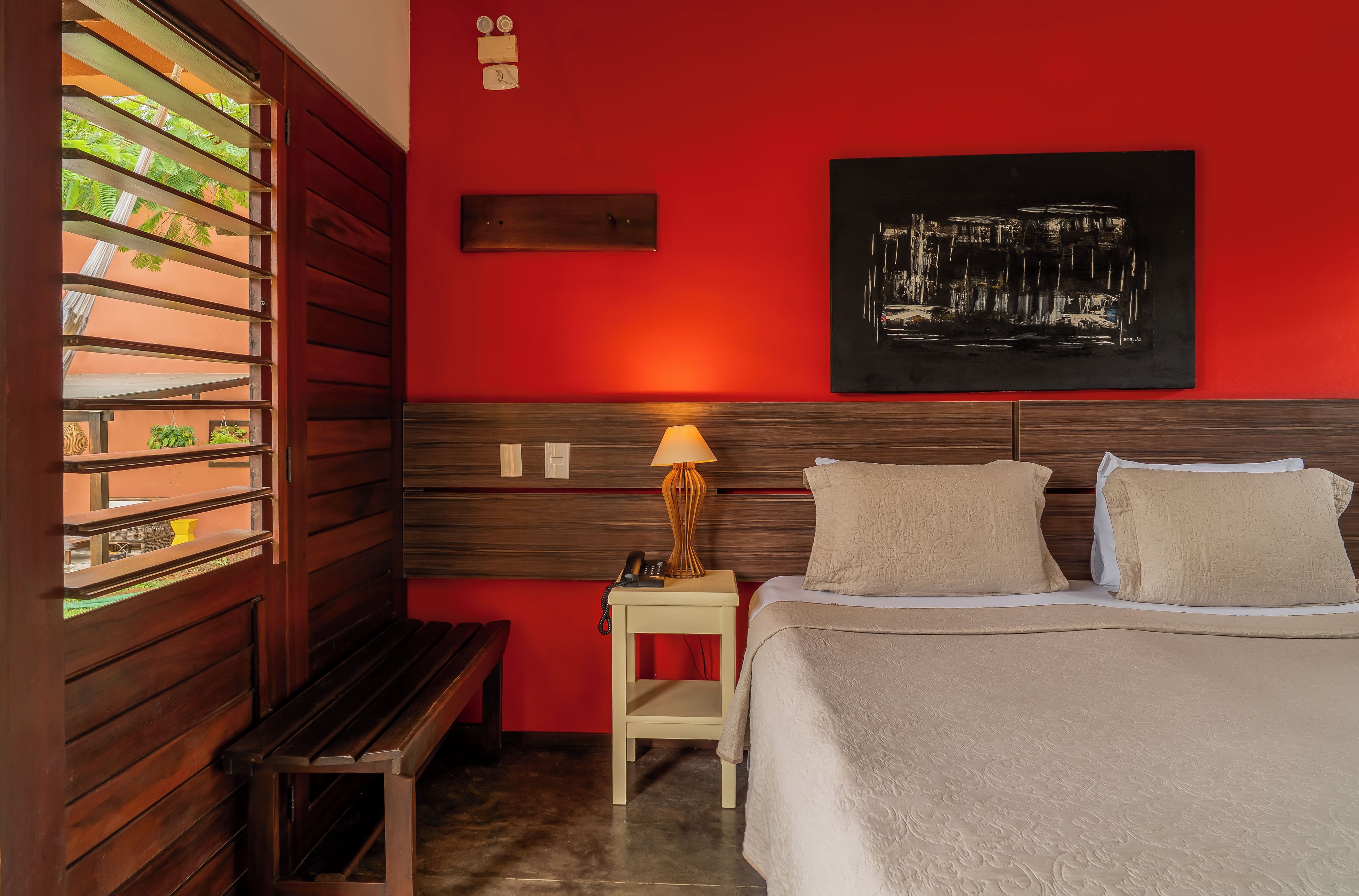 Una habitación de hotel con cama, mesita de noche, lámpara y un cuadro colgado en la pared.