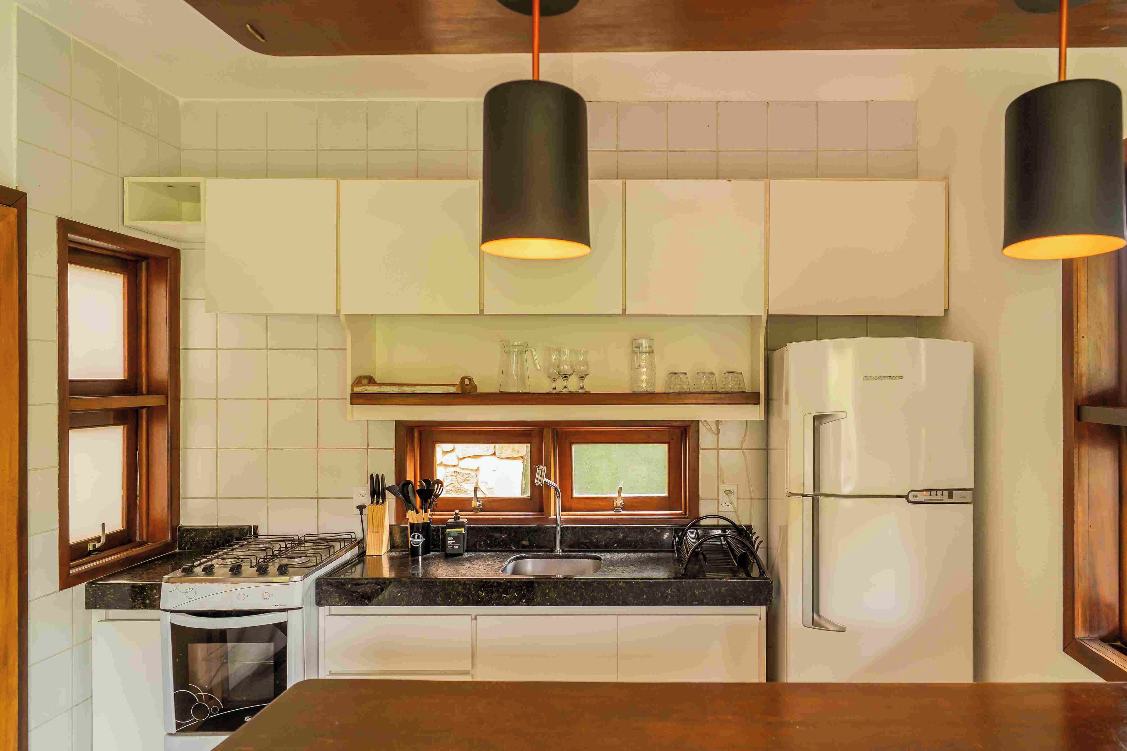 Cocina con estufa, horno, pileta y refrigerador. Hay lámparas colgantes y una ventana sobre la pileta.