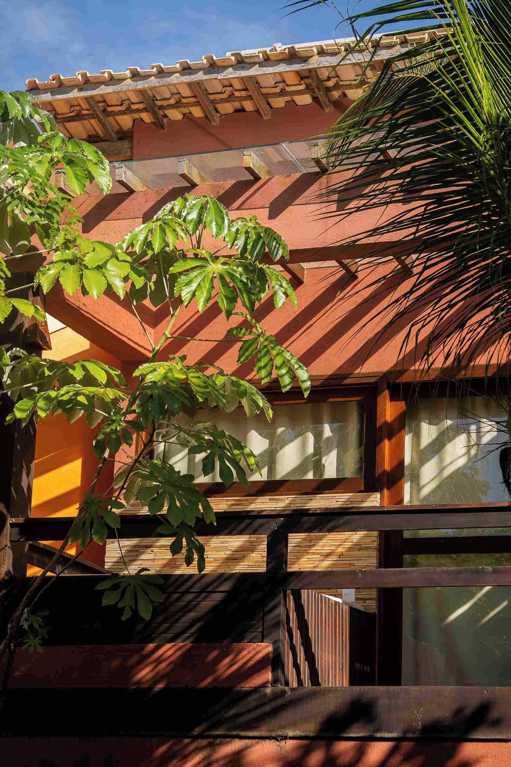 Un edificio con tejado de tejas, amplias ventanas y un árbol de hojas anchas en primer plano.