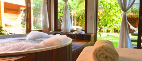 A spa area with a hot tub, towels, and a view of greenery through large windows.