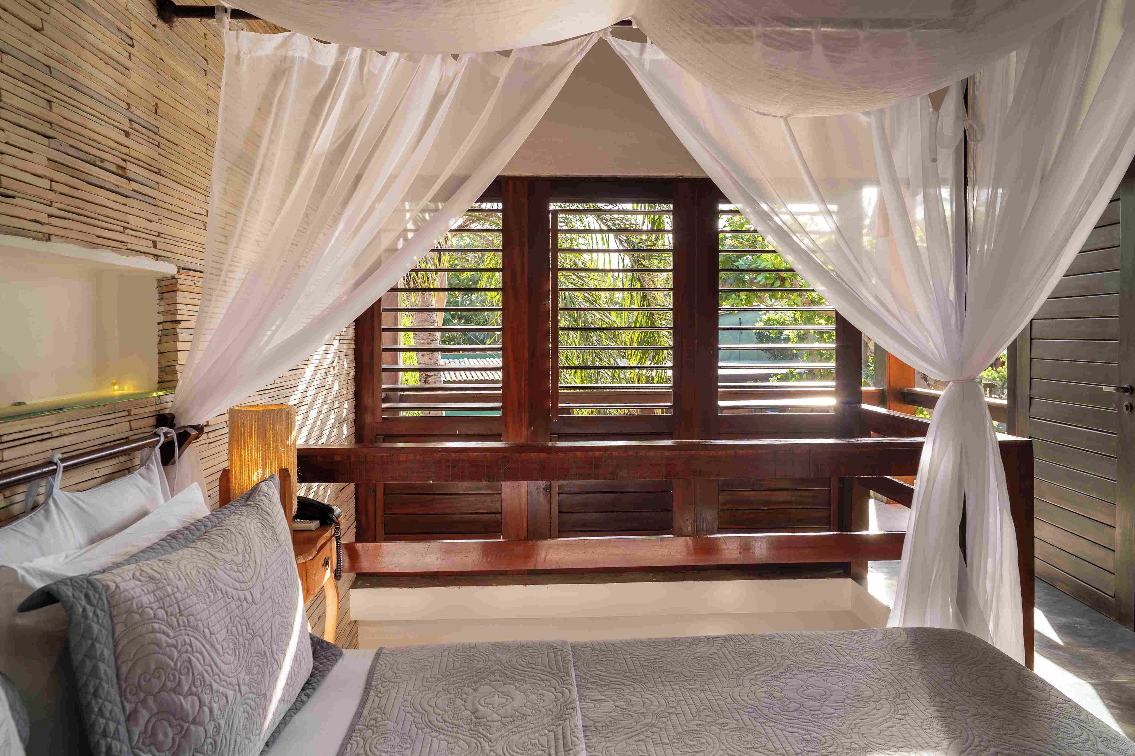 A bedroom with a bed, a nightstand, a lamp, and a window with a view of greenery.