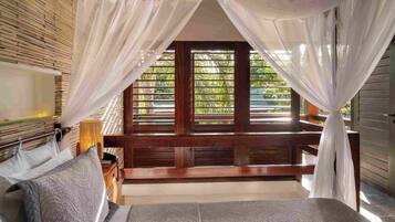 A bedroom with a bed, a nightstand, a lamp, and a window with a view of greenery.