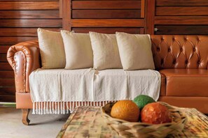 Un sofá de cuero marrón con una manta blanca y cuatro almohadones frente a una pared de madera.