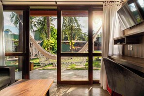 Una habitación con un amplio ventanal corredera que da a un jardín con una hamaca y palmeras.