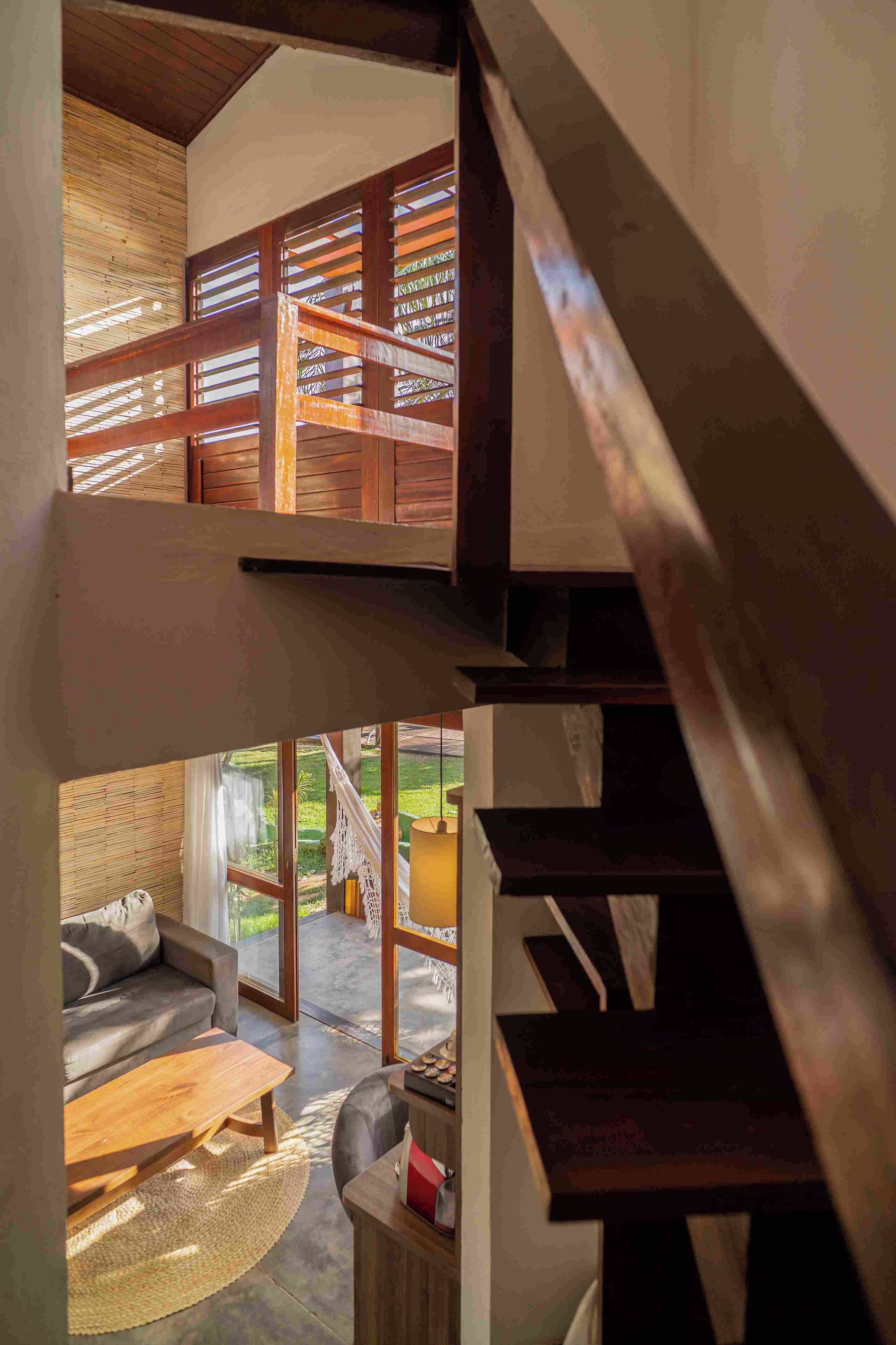A multi-level interior with a staircase, wooden beams, and a view of an outdoor area with a sofa and table.