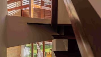 A multi-level interior with a staircase, wooden beams, and a view of an outdoor area with a sofa and table.