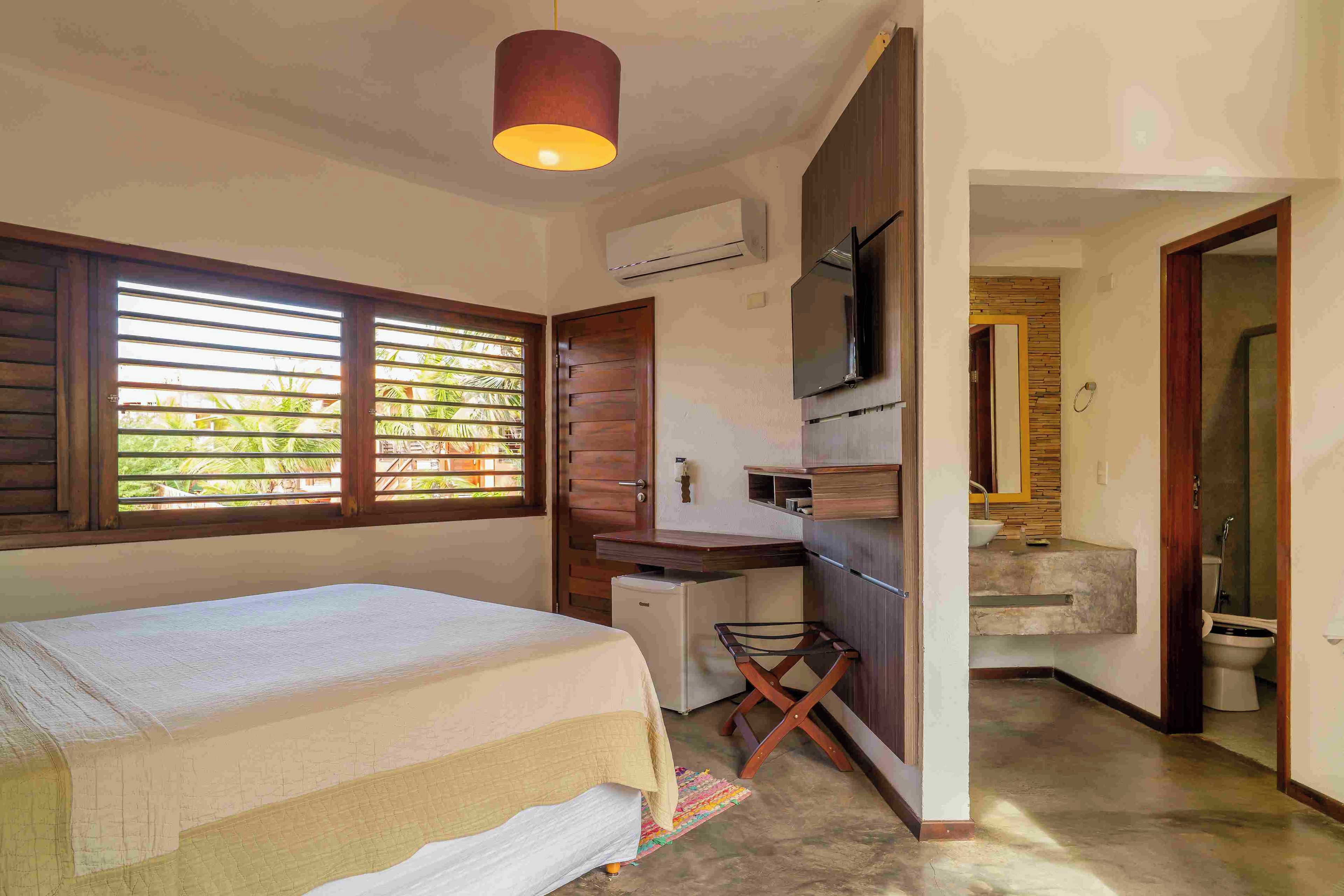 Un dormitorio con cama, escritorio, televisión y un baño a la vista a través de una puerta abierta.