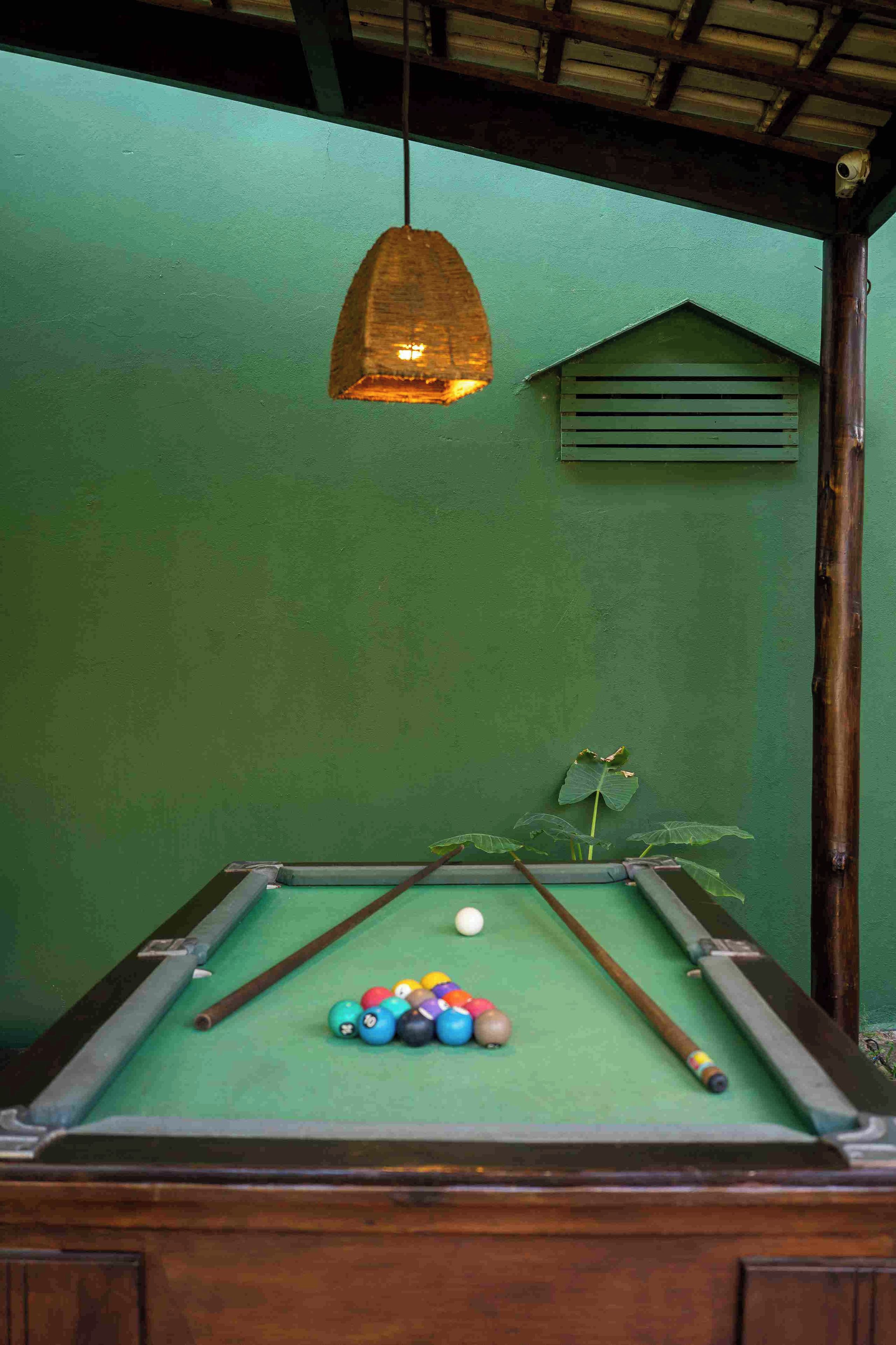 Una mesa de billar con bolas y tacos, una lámpara colgante y una pared verde.