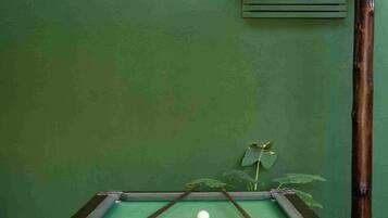 Una mesa de billar con bolas y tacos, una lámpara colgante y una pared verde.