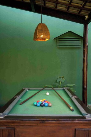 Una mesa de billar con bolas y tacos, una lámpara colgante y una pared verde.