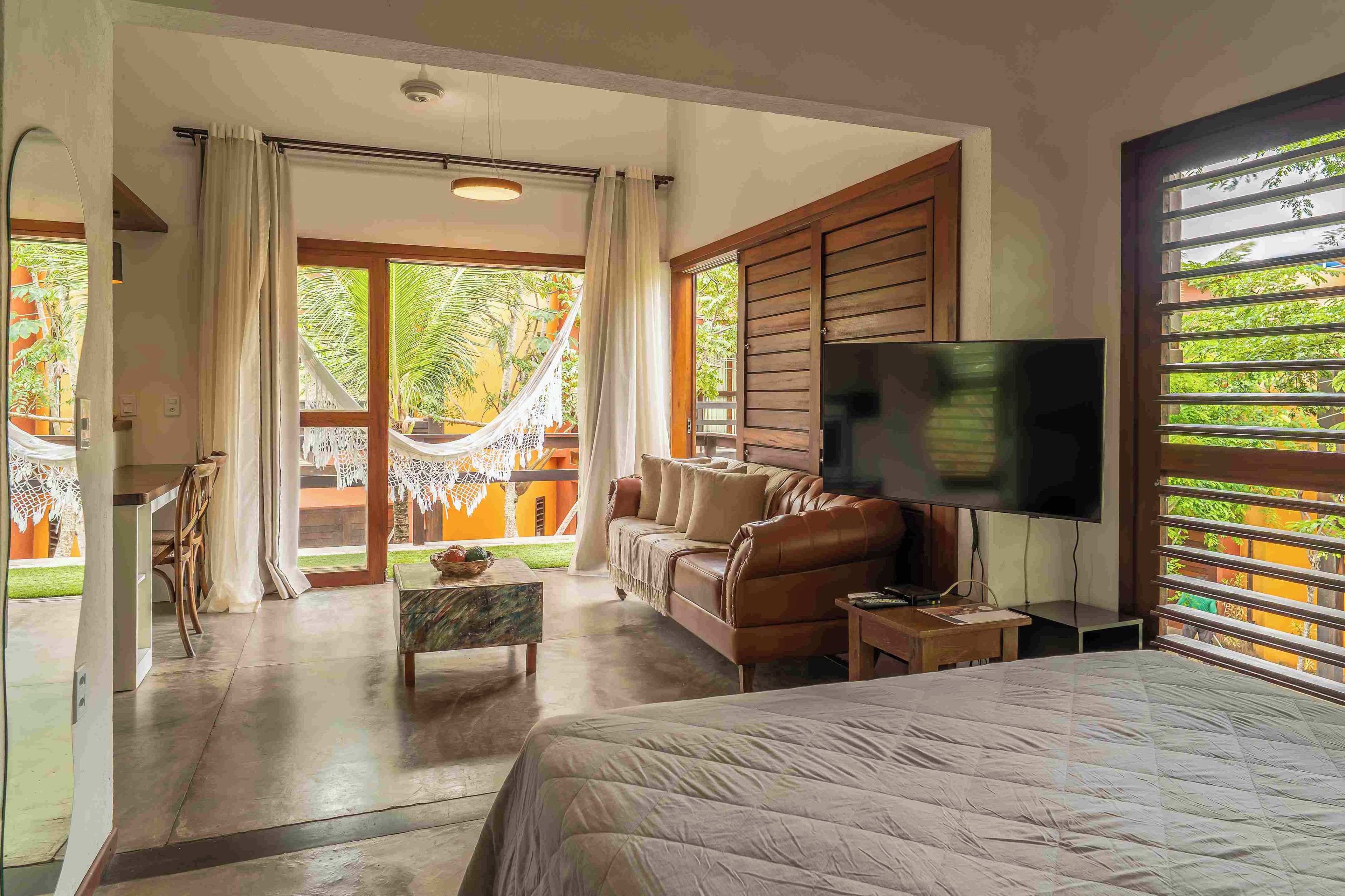 Un dormitorio con cama, televisor, sofá, mesa de centro y vista al exterior.