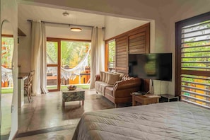 A bedroom with a bed, a TV, a sofa, a coffee table, and a view of the outdoors. - Pousada Naquela (Jijoca de Jericoacoara)