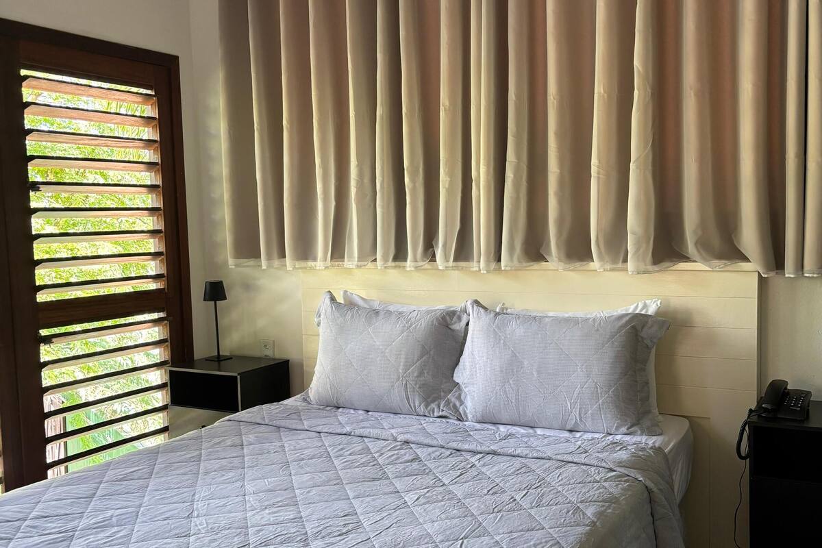 Une chambre à coucher avec un grand lit, une tête de lit agrémentée de rideaux, une table de chevet avec une lampe et un téléphone sur la table d’appoint.