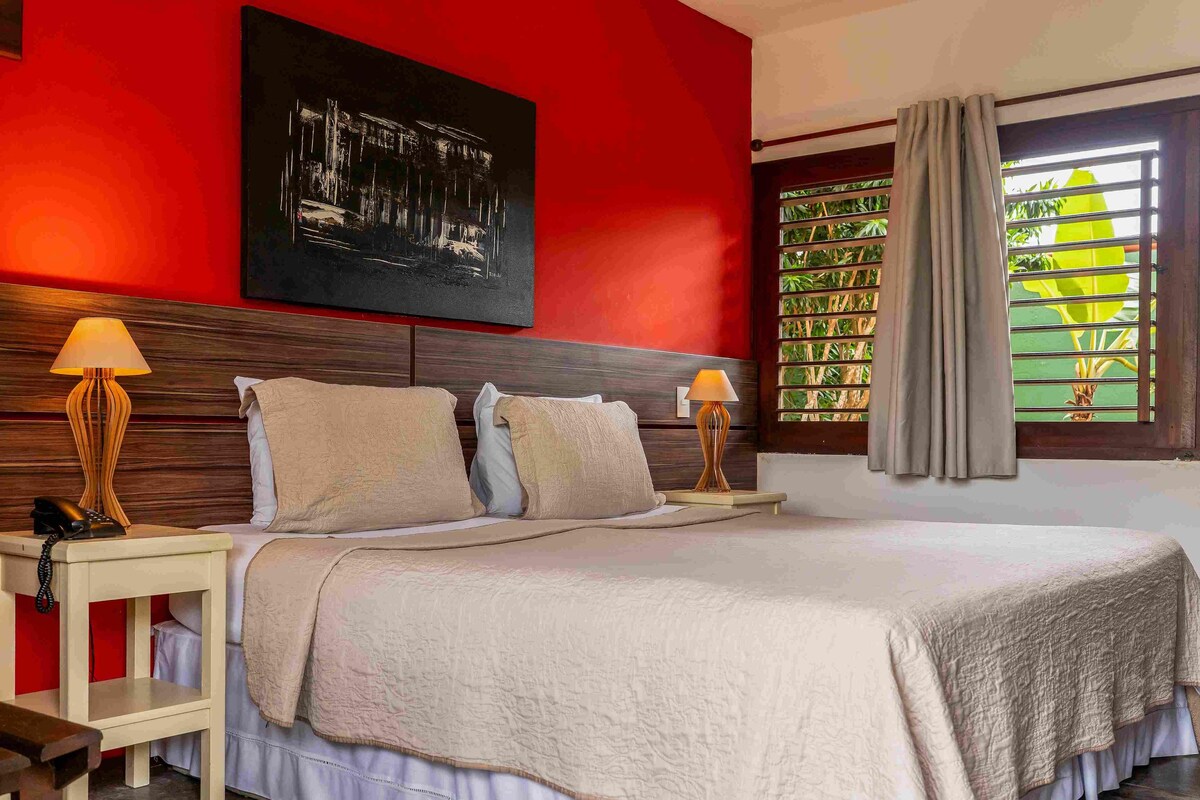 A hotel room with a large bed, two bedside lamps, a painting on the wall, and a window with curtains.