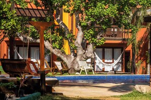 Un área de piscina con una hamaca, sillones de descanso y un gran árbol.