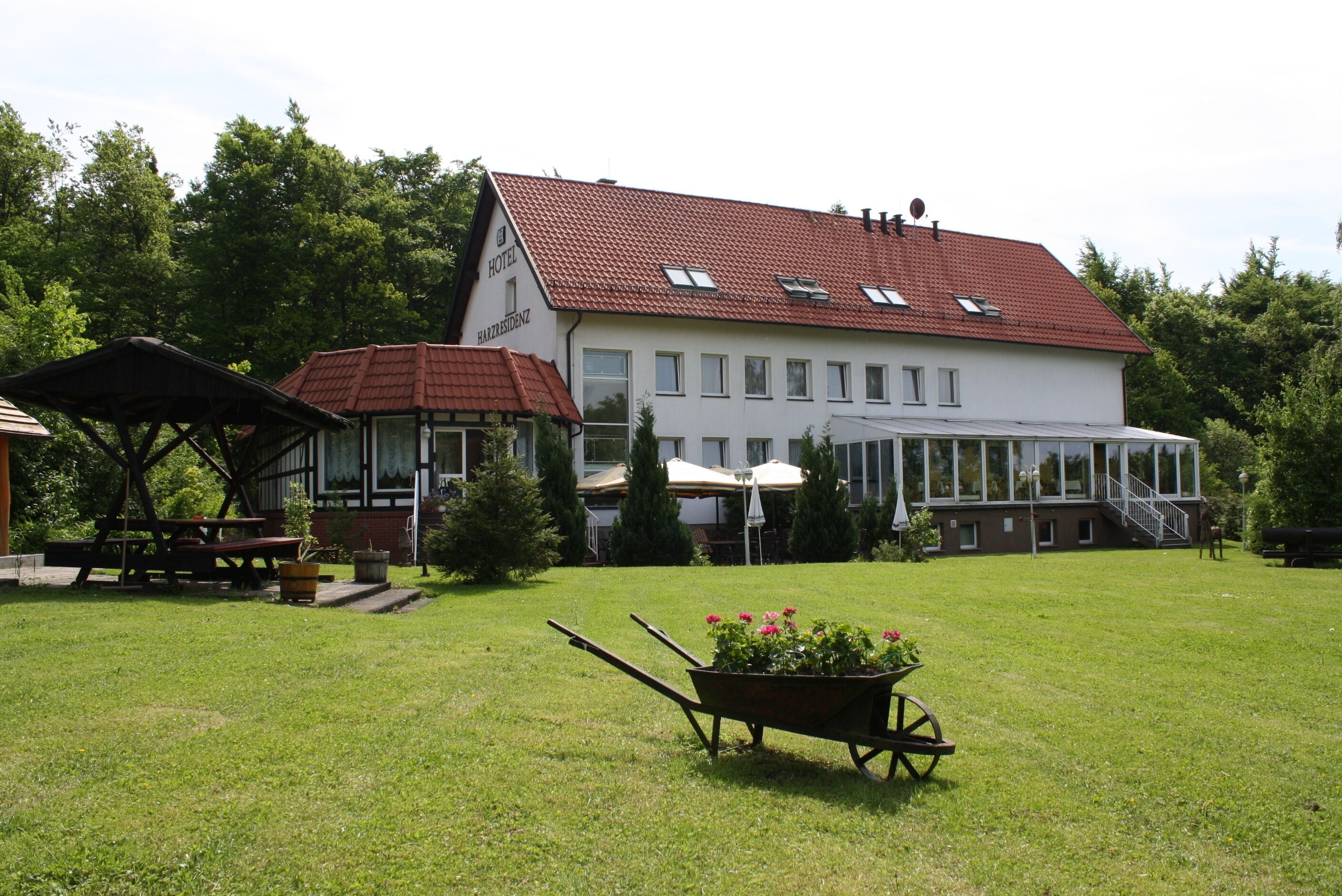 Ein Hotel mit rotem Ziegeldach, einer überdachten Außenbereich-Sitzgelegenheit und einer Rasenfläche mit einem Blumen-Bollerwagen.