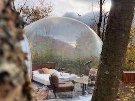 Una cúpula transparente cubre una habitación con una cama, sillas, una mesa y una lámpara.