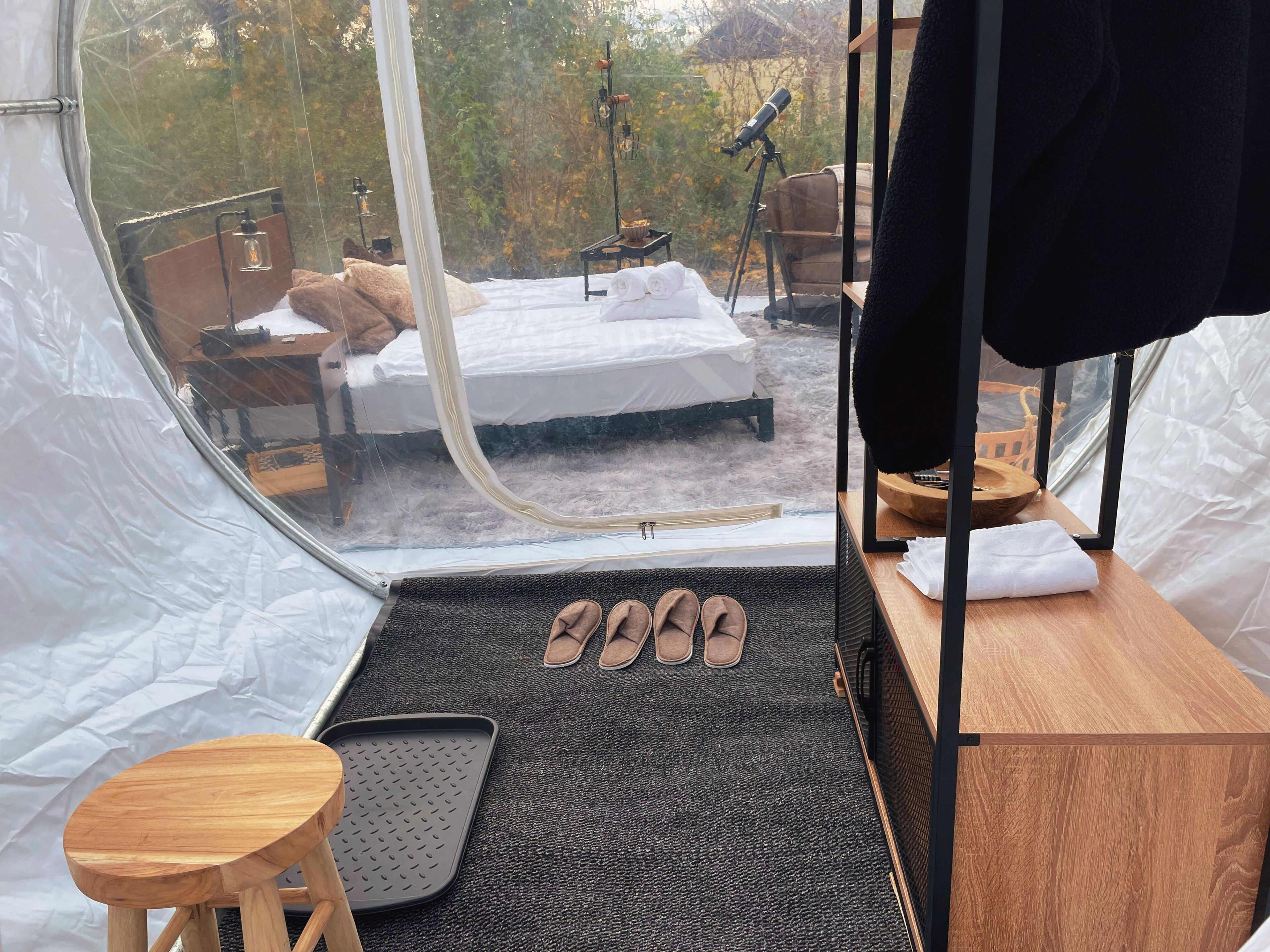 Eine Zeltunterkunft mit einem Bett, einem kleinen Tisch, einem Stuhl und Hausschuhen.
