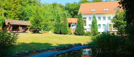 A hotel with a red-tiled roof, surrounded by lush greenery and a small pond.