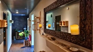 Un pasillo con pared de piedra, bancos de madera y un espejo con marco de piedra.
