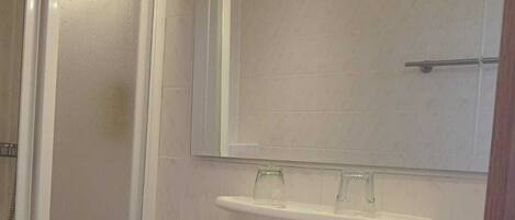Un baño con lavamanos blanco, un espejo y un cabezal de ducha de mano.