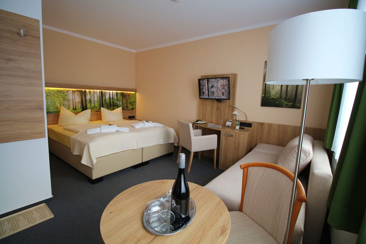 Habitación de hotel con cama, escritorio, sofá y mesa de comedor con una botella y vasos.