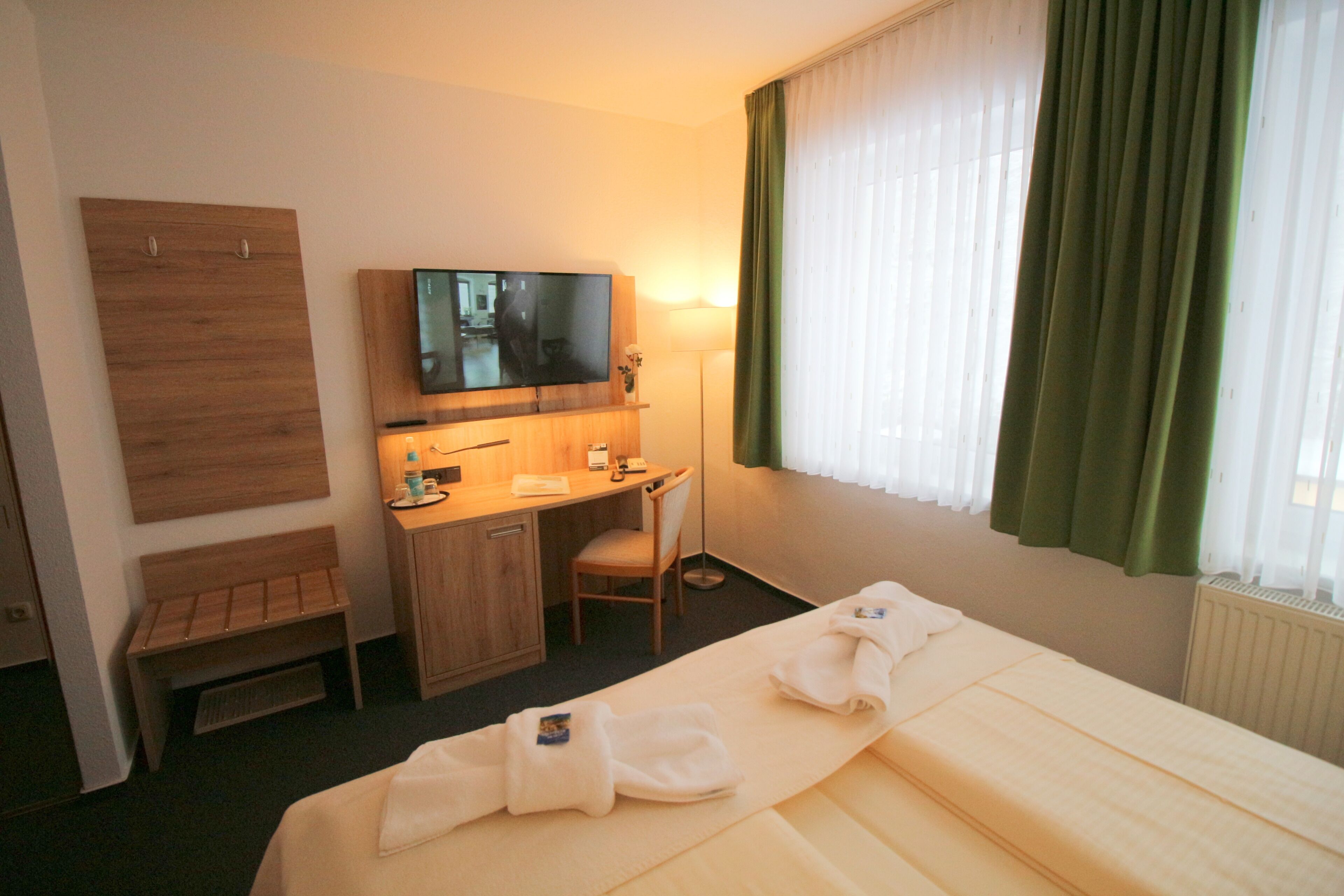 Ein Hotelzimmer mit Bett, Schreibtisch, Sessel, Fernseher und einem Fenster mit Vorhängen.