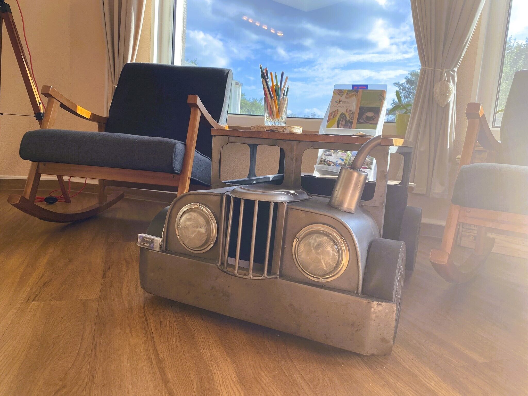 Une pièce avec un fauteuil à bascule, un bureau avec un ordinateur et une voiture jouet.