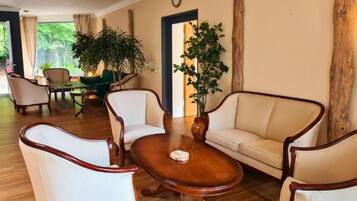A spacious living room with a wooden coffee table, two armchairs, a sofa, and a dining area with a green table and chairs.