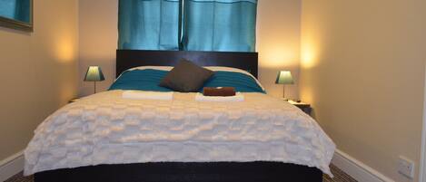 A neatly made bed with a white comforter and a dark headboard. There are two bedside lamps and a mirror on the wall.