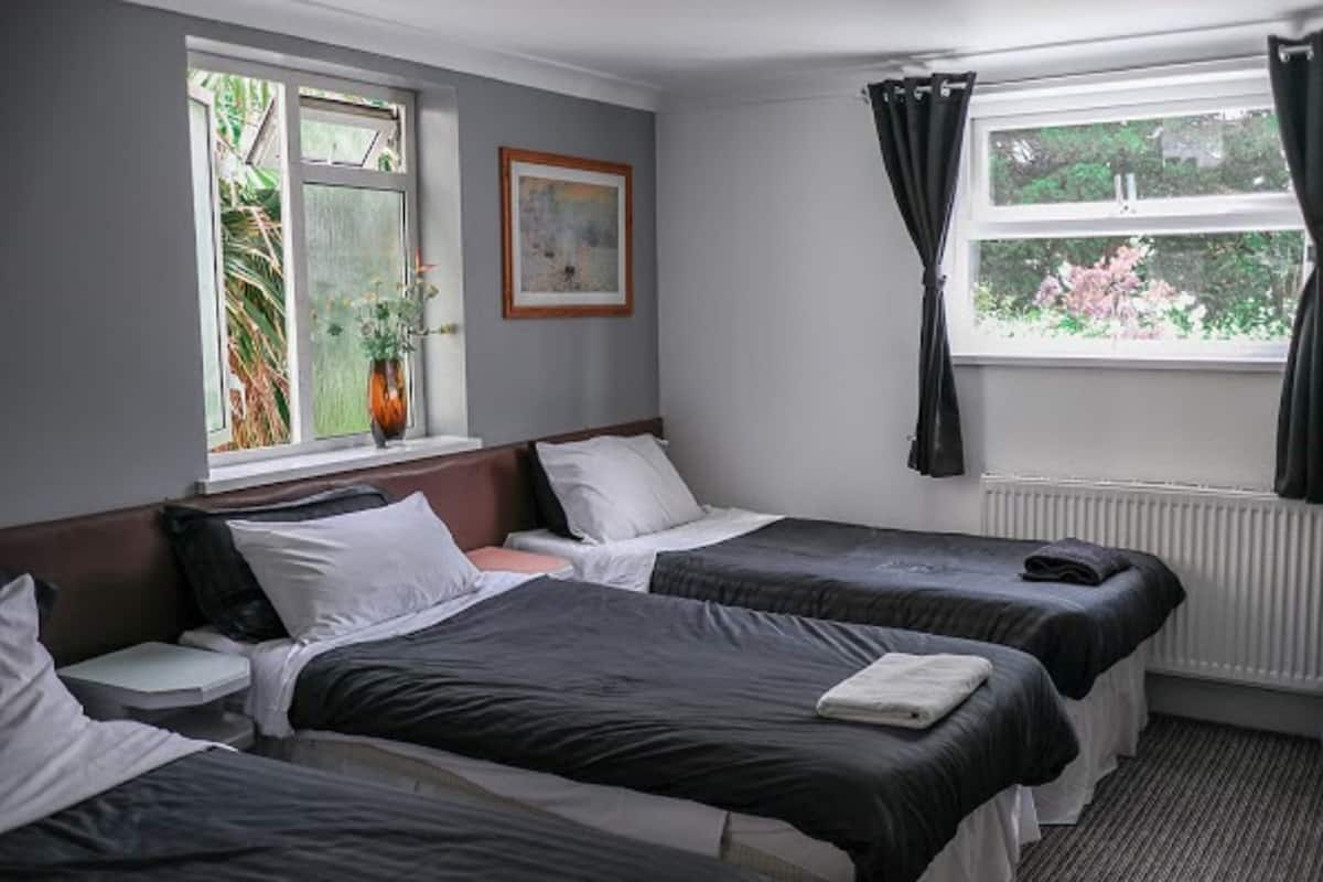 A hotel room with two beds, a window with curtains, a radiator, and a framed picture on the wall.