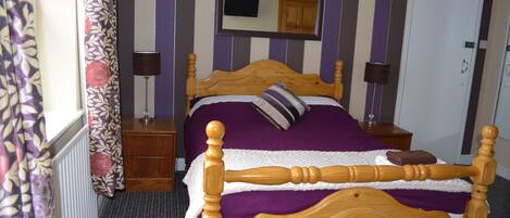 A wooden bed with a headboard, a bedside table, a lamp, a mirror, and a door in a room with striped walls.