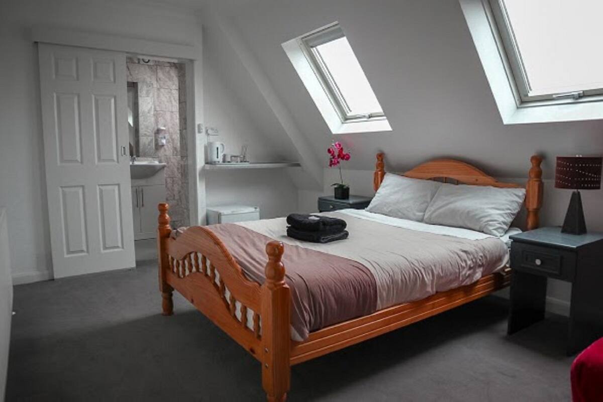 A bedroom with a wooden bed, a nightstand, a bedside table, a window, and a skylight.