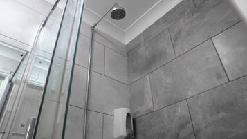 Un espace douche moderne doté d’une porte en verre, d’un pommeau de douche à main et d’un distributeur de savon fixé au mur.