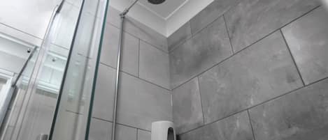 A modern shower area with a glass door, a handheld showerhead, and a soap dispenser on the wall.