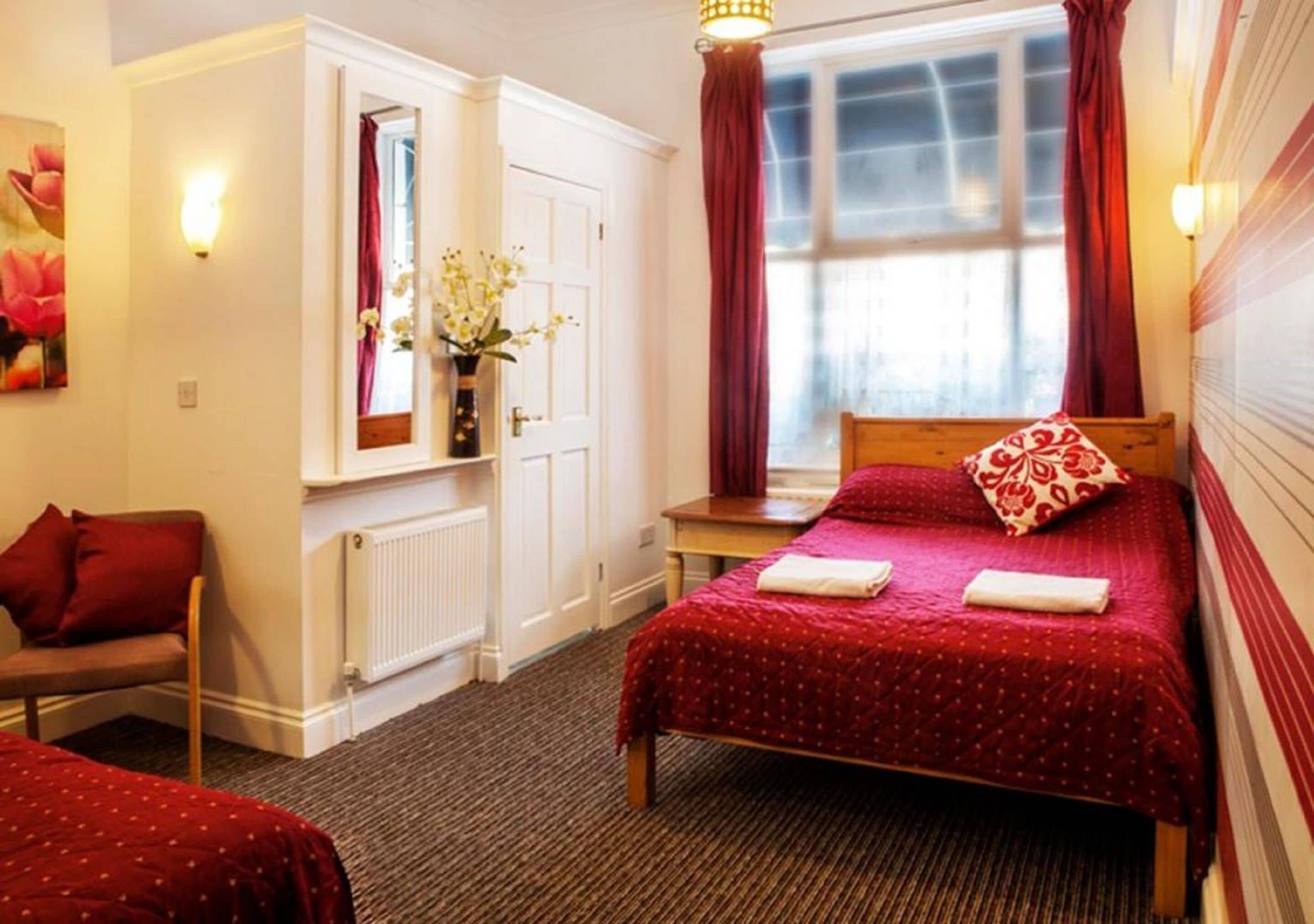 A hotel room with a bed, a chair, a small table, a window with curtains, and a radiator.