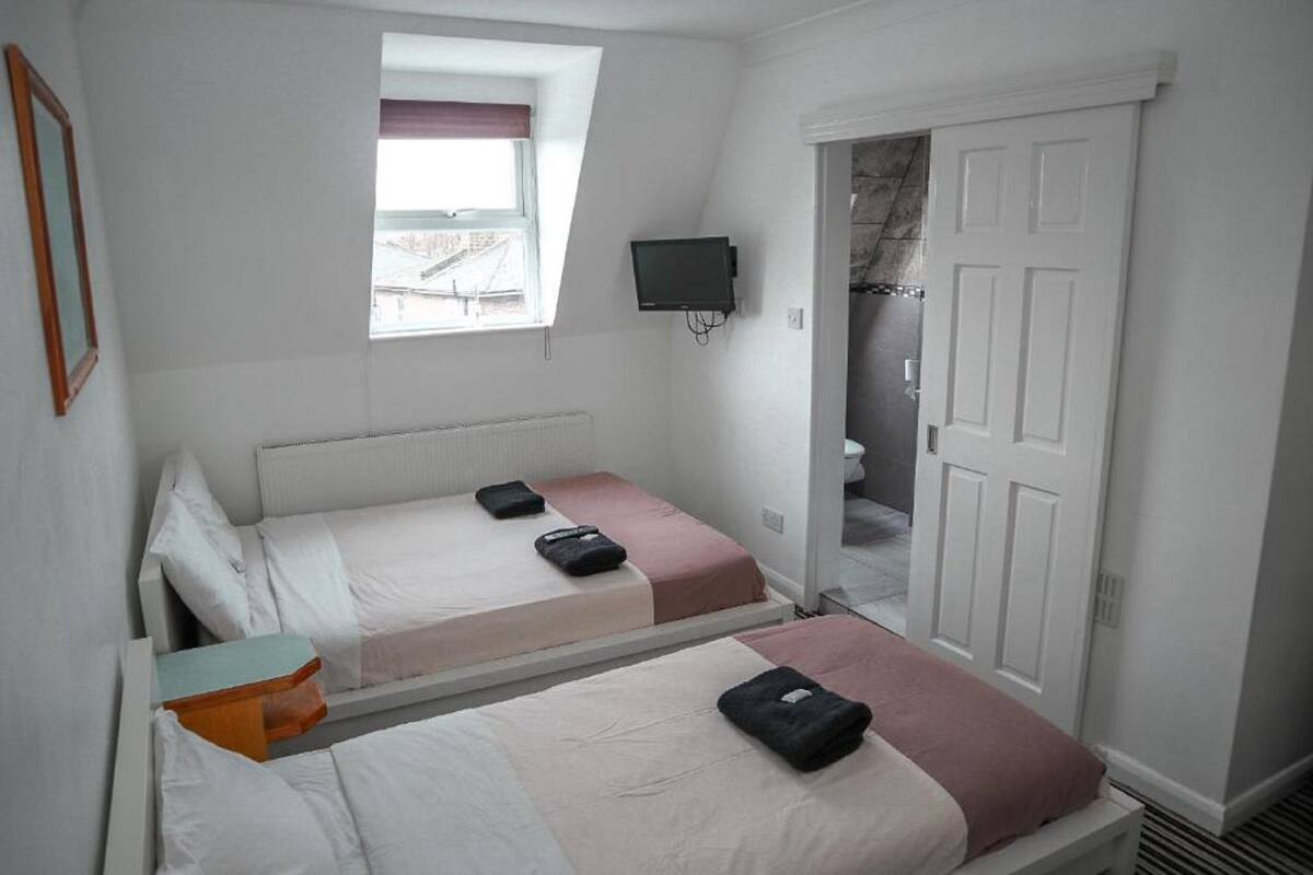 A bedroom with two beds, a TV mounted on the wall, and a door leading to a bathroom.